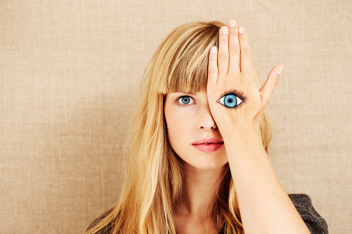 Dark Patterns: Eine Frau hält eine Hand vor ihr Auge, auf die ein zweites Auge gemalt ist