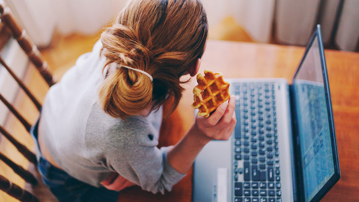 Cookies: Eine junge Frau sitzt am Laptop und isst eine Kekswaffel