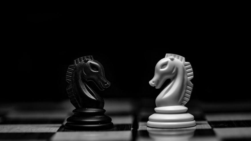 Eine weiße und eine schwarze Schachfigur (Springer) stehen sich auf einem Schachbrett gegenüber