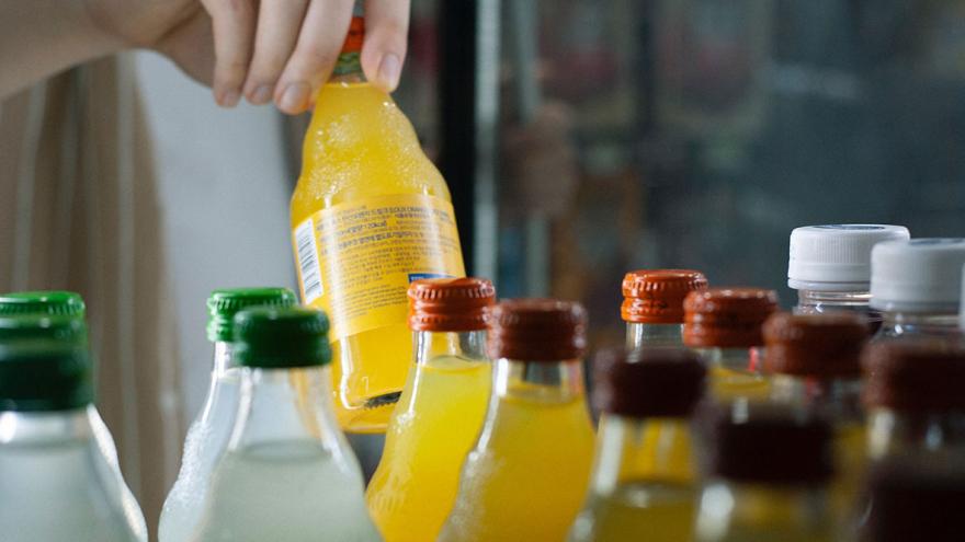 Ein Hand nimmt eine Flasche Limonade aus einem regal mit unterschiedlichen Getränkeflaschen