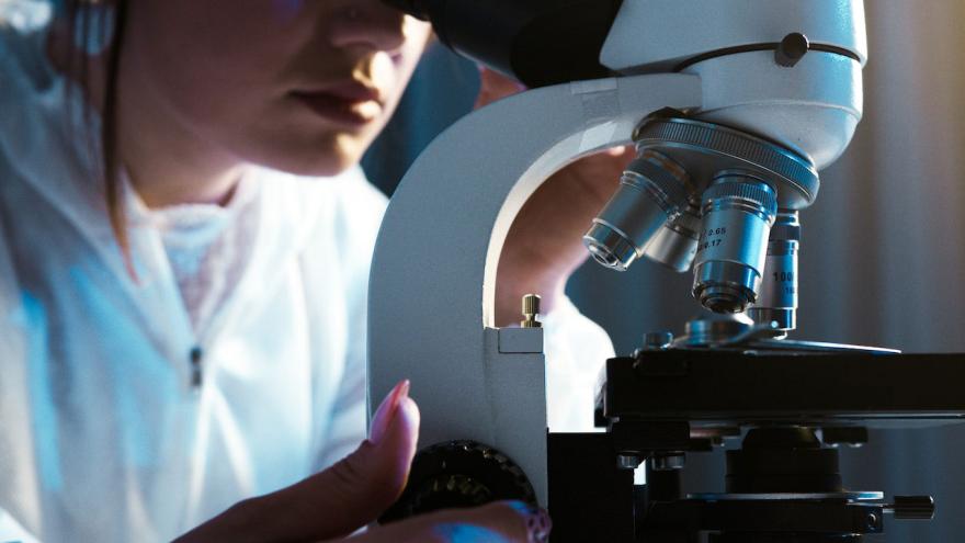 Eine Frau in Laborbekleidung untersucht etwas an einem Mikroskop